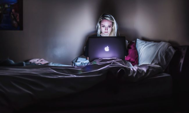 kvinna sitter med dator i sängen